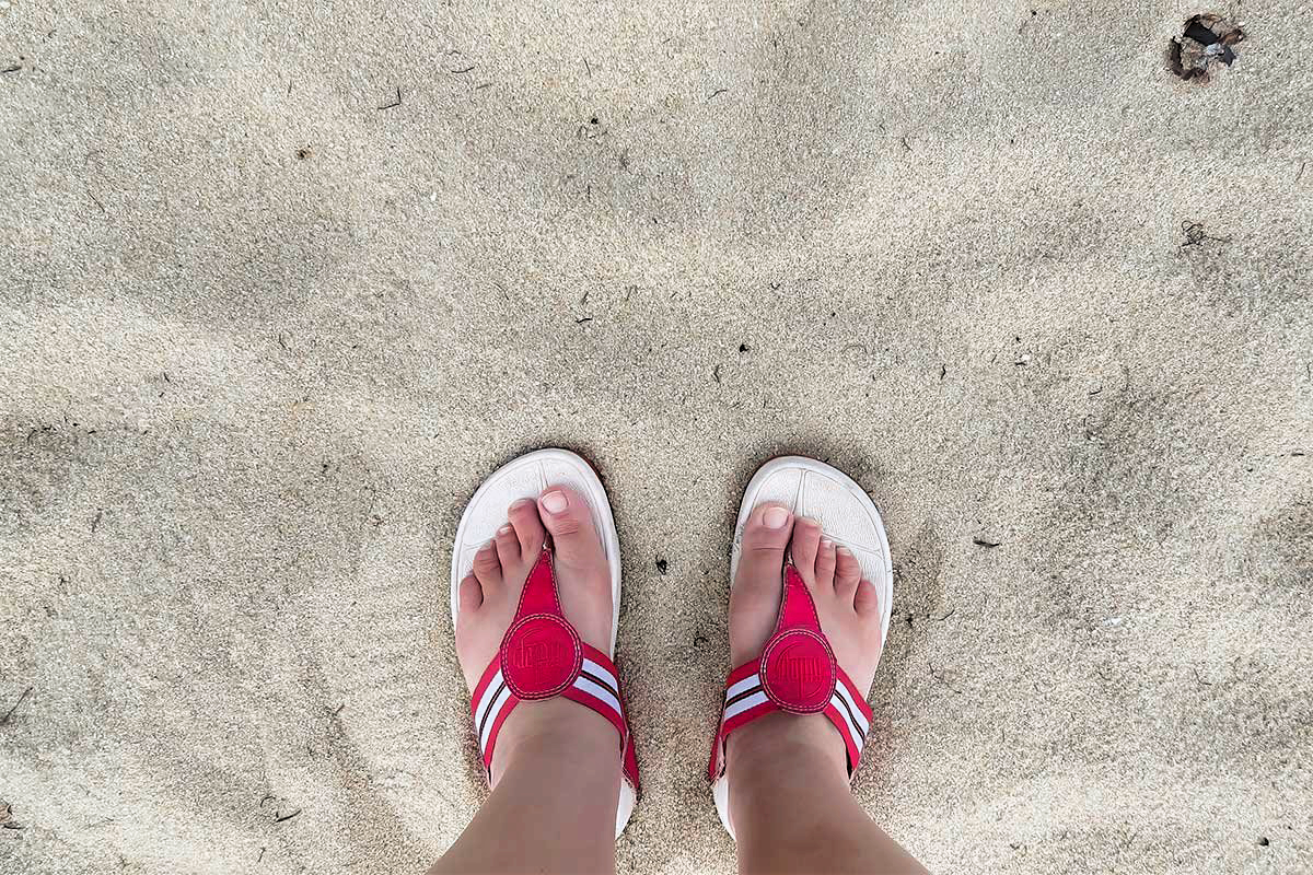 Belize-Family-Adventure-Travel-Guide Close-up of two feet in red sandals resting on the white sand beaches of Belize — a relaxing moment from a Belize Family Adventure Travel Guide experience.