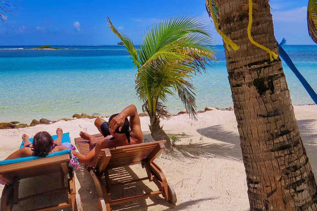 Couple-in-Belize - Authentic Travel Belize Couple relaxing in beach chairs on white-sand shore with turquoise Caribbean waters in the background — perfect setting for Belize vacation packages for couples.