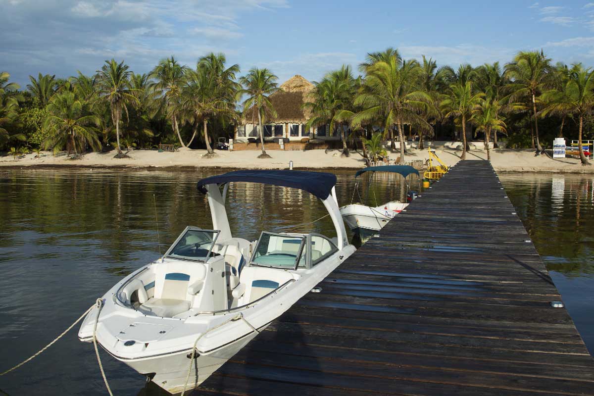 Secluded-Island-Lodge - Authentic Travel Belize Secluded island with a private villa, coconut trees, white sand beach, and a luxury boat docked over turquoise waters — Belize vacation packages for couples