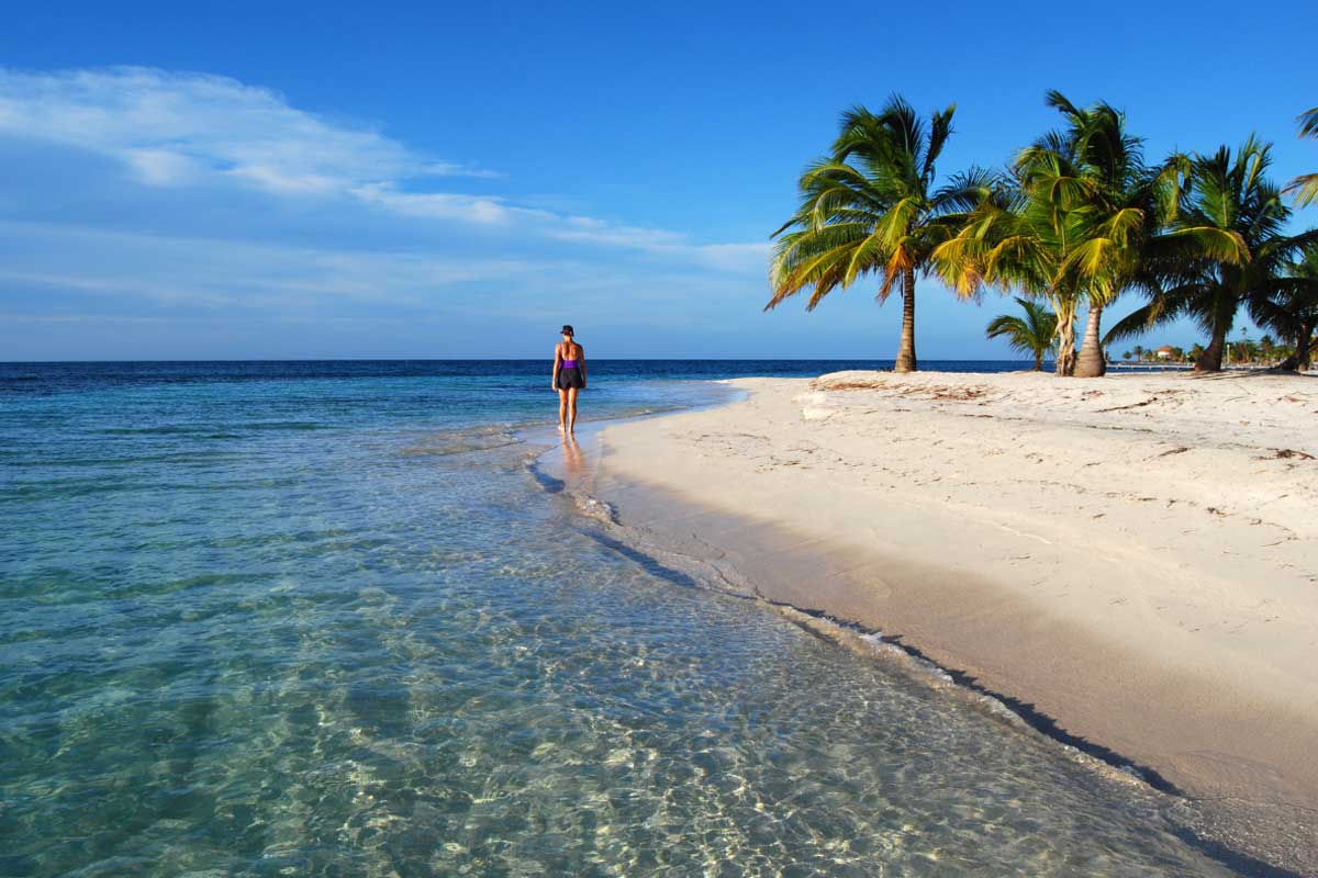Woman walking along secluded white-sand beach with turquoise waters during a luxury package holiday to Belize