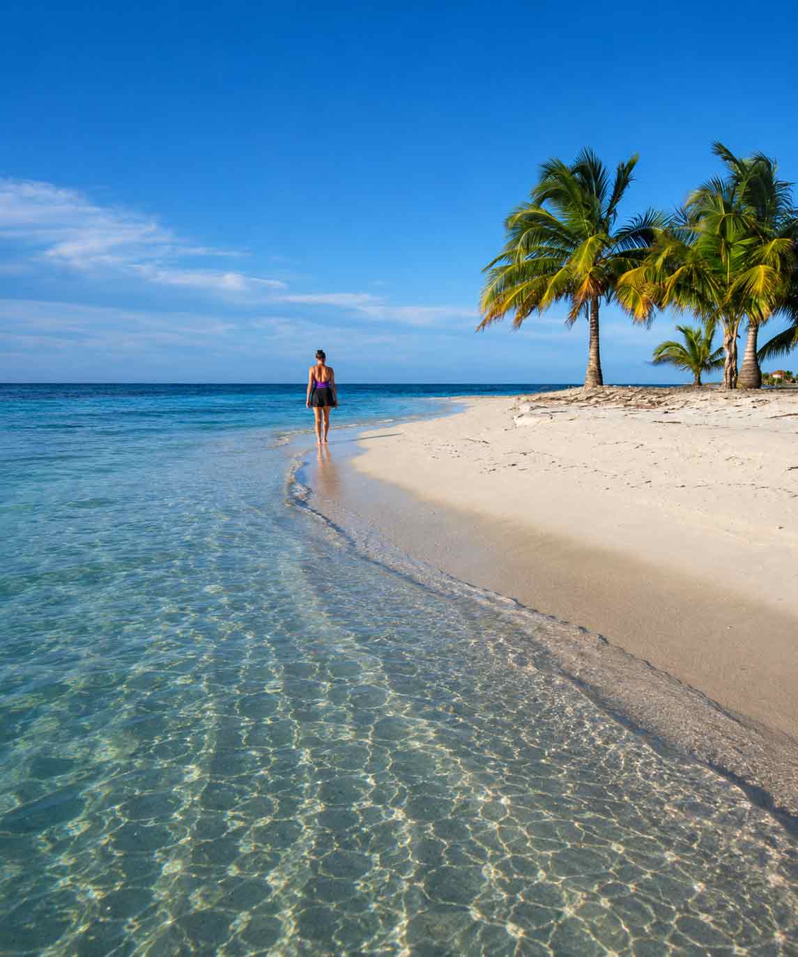 Belize-Atoll - Authentic Travel Belize Woman walking along a secluded tropical beach during a Belize Sailing Vacations escape with crystal-clear Caribbean waters and palm trees in Belize.