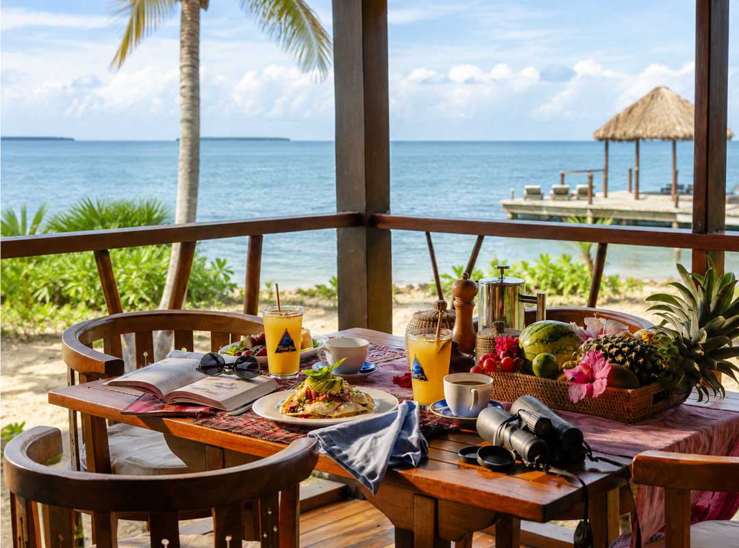 Placencia-Lodge-Breakfast - Authentic Travel Belize Tropical breakfast with fresh fruit and coffee served at a corner table overlooking the Caribbean Sea in Placencia, Belize.